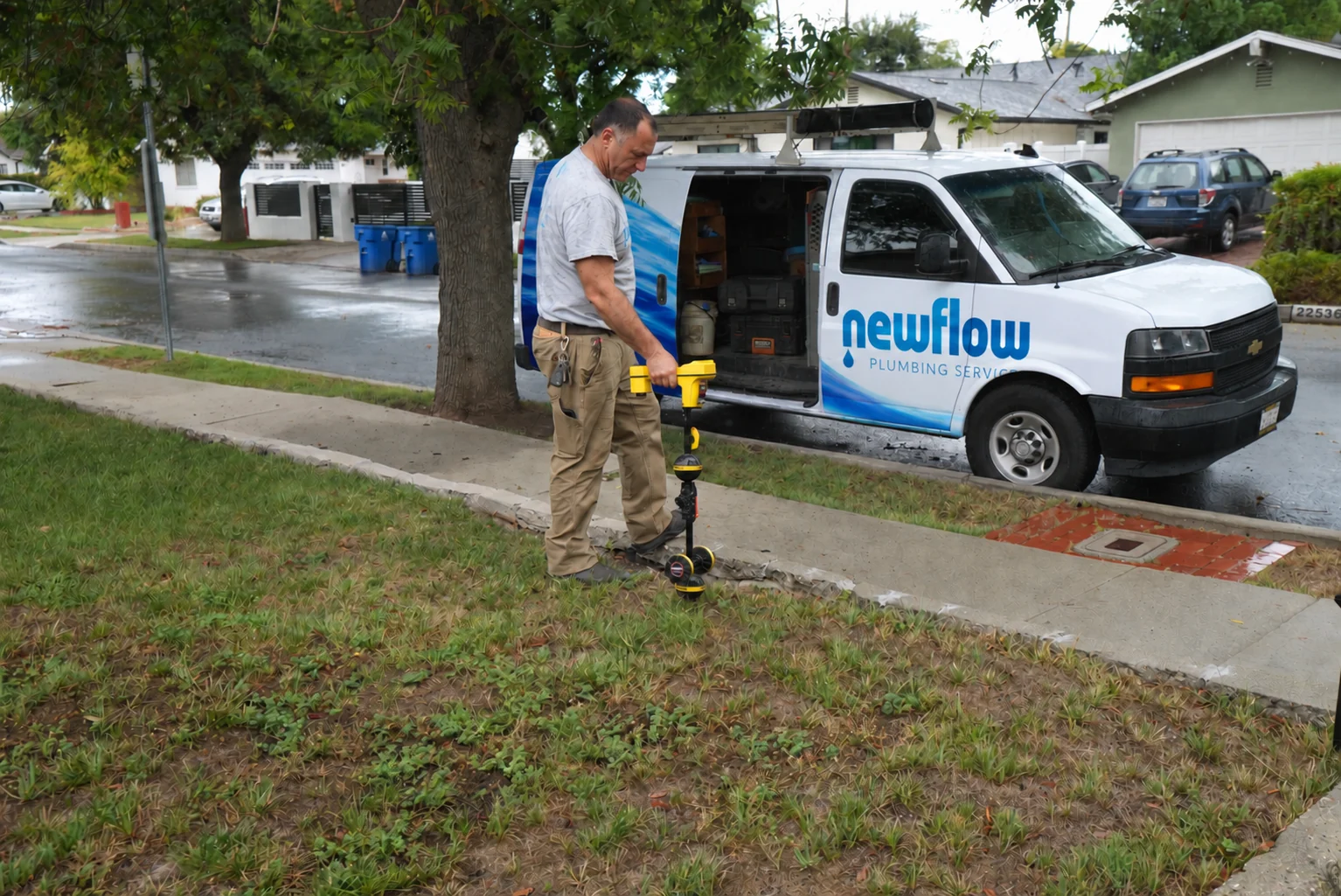 New Flow Plumbing technician using professional pipe locating equipment beside a branded service van