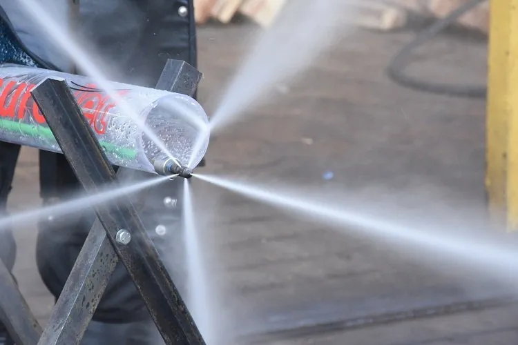 Close-up of a high-pressure hydro-jetting nozzle inserted into a clear plastic test pipe, blasting multiple powerful white water jets radially outward in a perfect 360-degree starburst pattern during a demonstration.